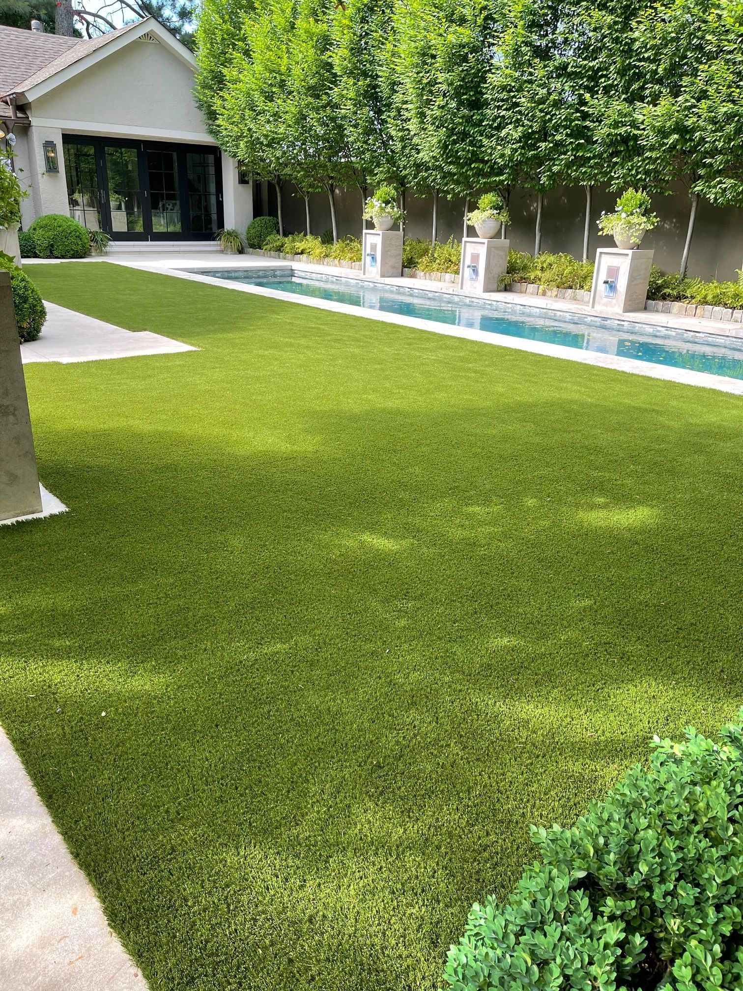 Manicured lawn running alongside a linear pool with potted topiaries